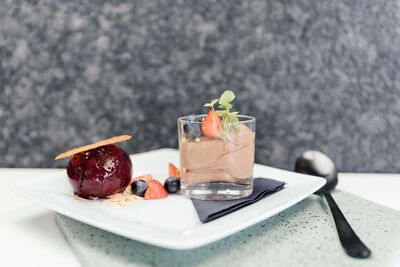 Een wit bord met een glaasje met chocolade mousse en een bolletje rood ijs met vruchtjes ernaast