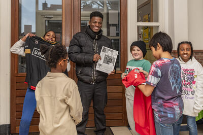 Een profvoetballer poseert met glimlachende kinderen die trots een krant tonen