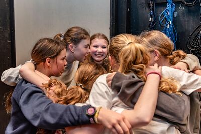Een groep leerlingen omarmt elkaar vol spanning en plezier voor hun optreden