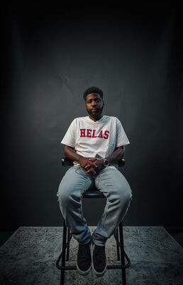 Man zit op een kruk in een donkere studio en kijkt rustig in de camera.