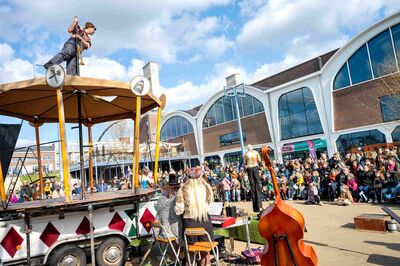 Grote buitenvoorstelling met muzikanten op een verhoogd podium en publiek dat in een halve cirkel om de scène staat.