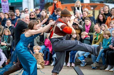 Acteurs spelen een energieke scène midden in het publiek, waarbij een speler wordt voortgeduwd en toeschouwers dichtbij reageren.