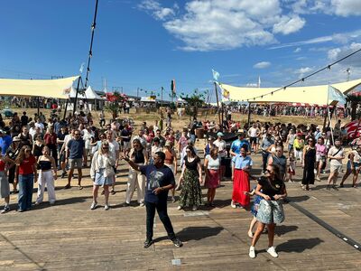 Grote groep mensen volgt een dansworkshop in de zon op een houten vloer aan de Waal.