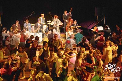 Drukke dansvloer met koppels die samen dansen voor een live band op het podium.