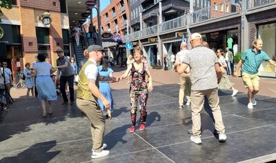 Dansworkshop in de Marikenstraat van Nijmegen waarbij deelnemers samen dansen op een plein tussen winkels.