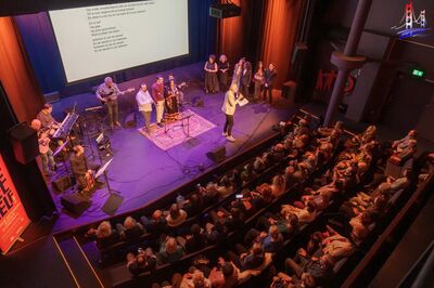 Volle theaterzaal waar muzikanten optreden en het publiek aandachtig luistert.
