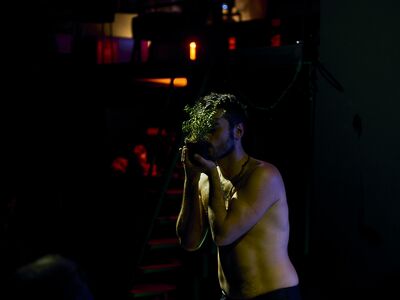 A shirtless man is holding a plant tenderly against his head.
