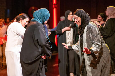 Twee vrouwen in lange jurken dansen tegenover elkaar, omringd door andere dansende bezoekers in een warme, sfeervolle zaal