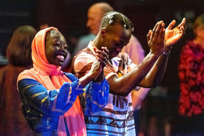Twee mensen lachen en klappen enthousiast mee tijdens een optreden. Ze staan dicht bij elkaar en stralen plezier en verbondenheid uit.