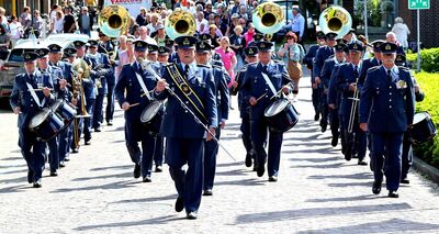 Een fanfare loopt spelend de camera tegemoet. Achteraan lopen mensen enthousiast met hen mee.